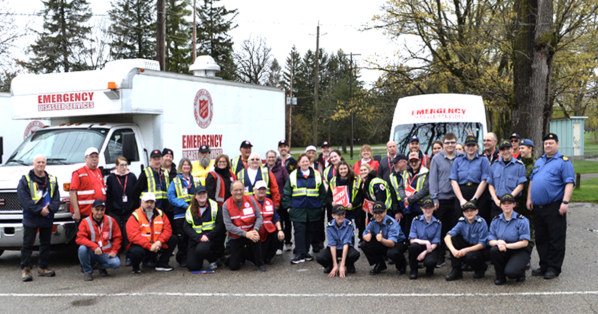 A group of cadets and Salvation Army workers in front of two emergency disaster services vehicles